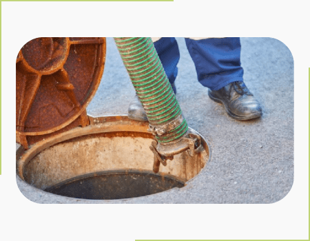 A man standing next to a grease trap with a vacuum hose.