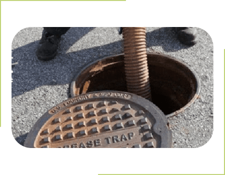 A man next to a manhole cover pumping out a grease trap.